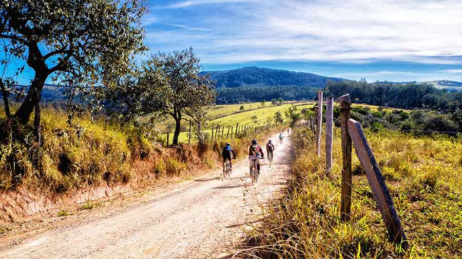 A group of people is mountain biking around Sicily on a sunny day, relishing the beautiful scenery and weather.