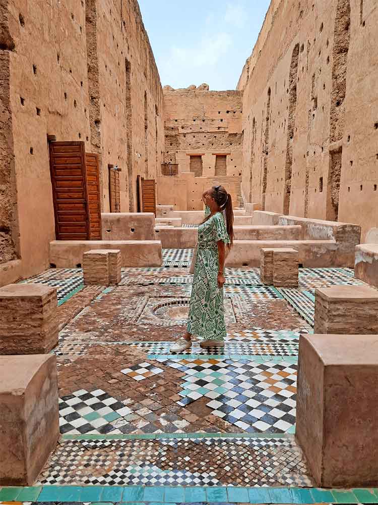 A woman (me) wearing a long pattered white and green dress. Stood on a mozaic floor in a ruin of a palace in Marrakech. This image is an example of what to wear in Marrakech (& Morocco) as a woman.