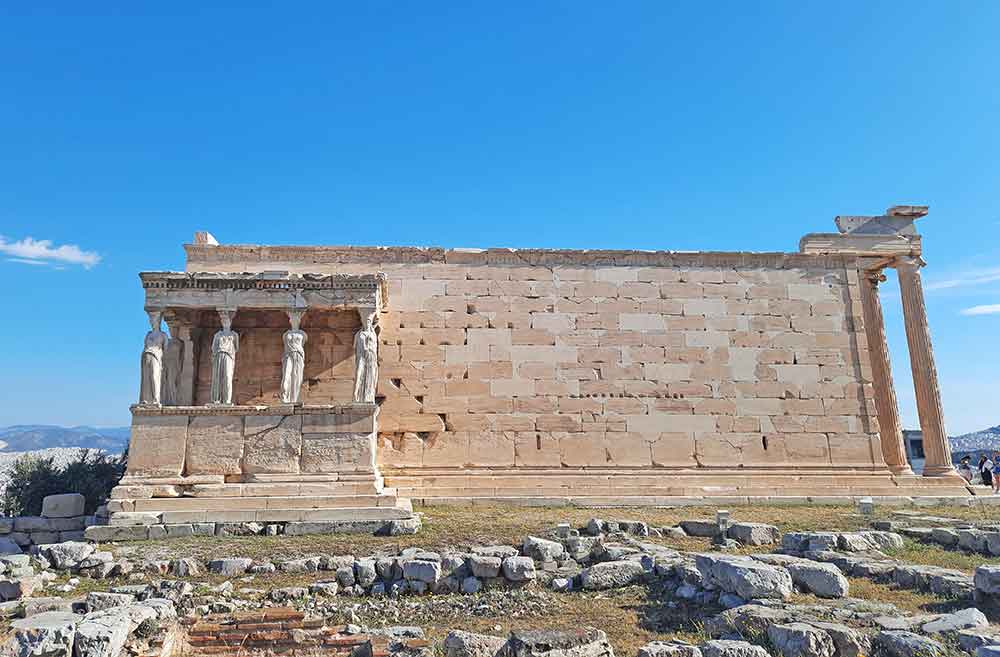 The Erechtheum building features brick walls with statues standing on the side of the wall