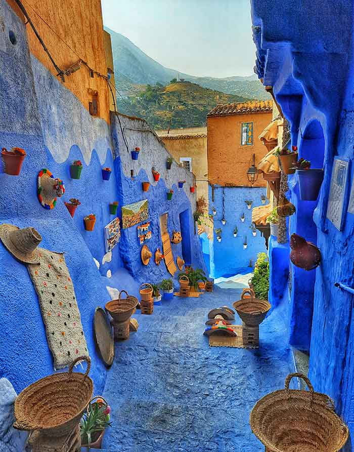 Chefchaouen - the street captivate with its stunning blue hues, as the walls and hallways are painted in various shades of blue together with a baskets and hats placed on the street - and the Spanish Mosque in the background