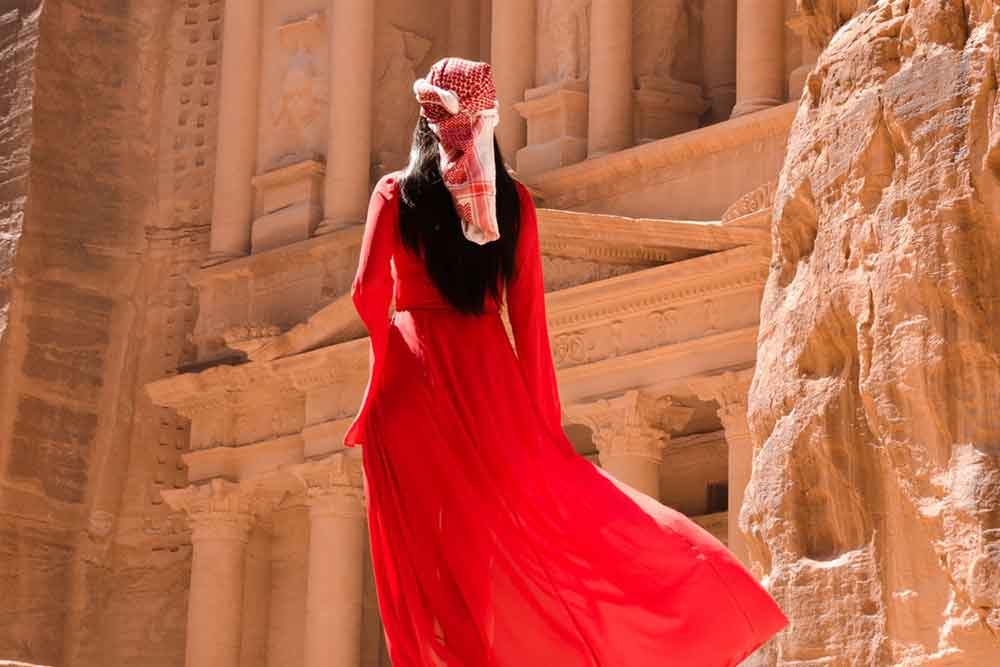 Woman wearing a red maxi dress and scarf infront of Treasury, Petra, Jordan on a sunny day