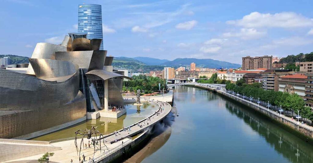 Image of the abstract shaped Guggenheim Musuem steel facade and the Nervion River. Discover is Bilbao worth visiting in this article.