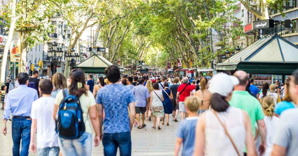 Crowds of tourists walking along La Rambla in Barcelona on a busy summer day, highlighting the worst time to visit Spain due to overcrowding.